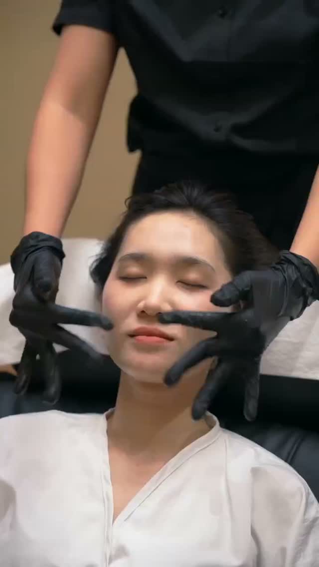 A client receiving a facial or scalp massage from a gloved therapist.